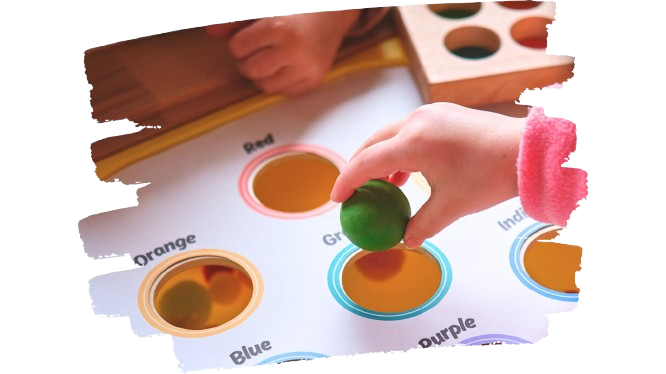 A kid dropping a green wooden ball into a hole from the VIPrint Studio multi-use color sorting insert.